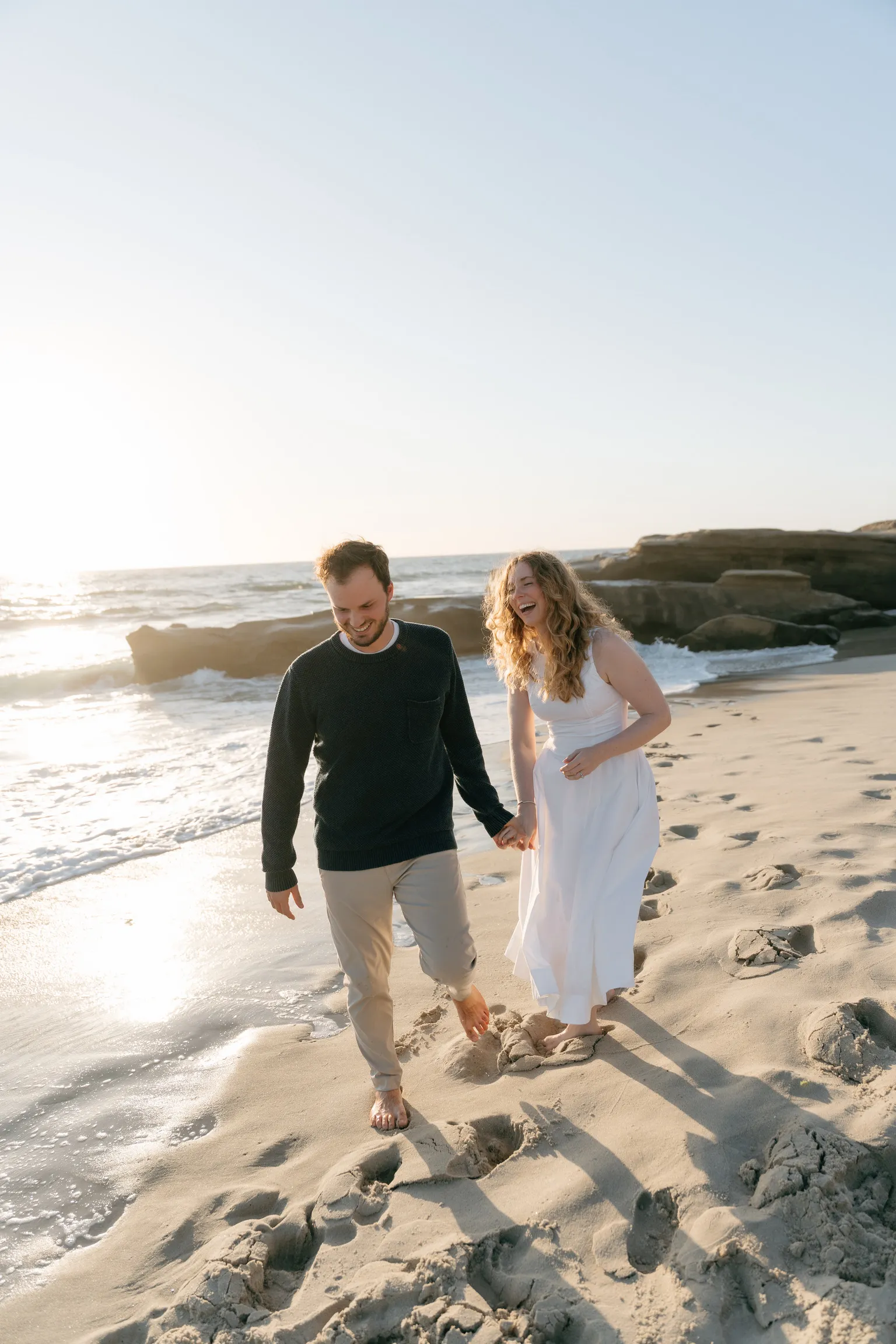 Natalie and Tyler laughing while walking barefoot on the sand.